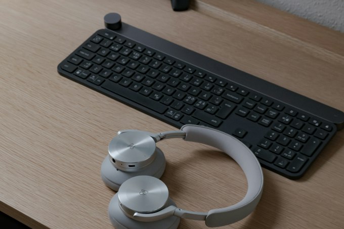 A keyboard and a pair of over-ear headphones on a wooden desk